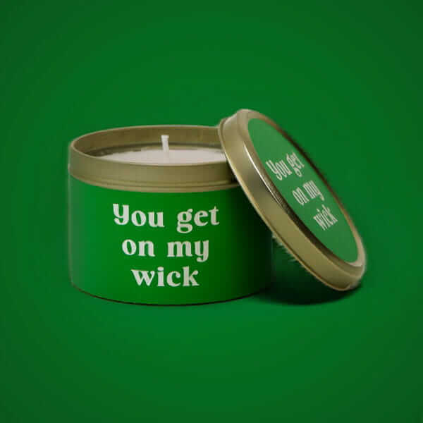 Novelty candle in a green tin with a humorous slogan, displayed against a green background.